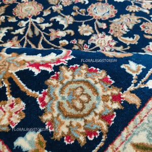 May include: Close-up of a navy blue rug with an intricate floral pattern in shades of beige, red, and light blue. The rug features a detailed design with scrolling vines and stylized flowers. The text "FLORALRUGSTOREIN" is visible.