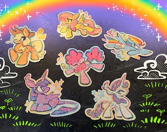 Può includere: Una collezione di adesivi di pony dei cartoni animati colorati con accenti glitterati. Gli adesivi presentano vari pony in pose diverse, su uno sfondo con un arcobaleno, nuvole e stelle.
