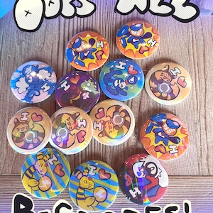May include: A collection of colorful round buttons with various cartoon character designs. The buttons feature vibrant colors like blue, orange, yellow, and purple, with the text "ODDS ALL" and "B-GRADES!" in a playful font.