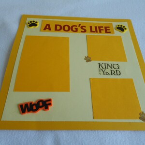 May include: A yellow scrapbook with a white background and the text "A Dog's Life" in red. There are paw prints and the text "King of the Yard" in black. The scrapbook has a yellow border and the word "Woof" in orange.