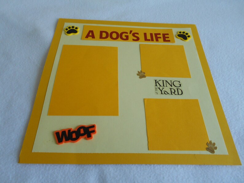 May include: A yellow scrapbook with a white background and the text "A Dog's Life" in red. There are paw prints and the text "King of the Yard" in black. The scrapbook has a yellow border and the word "Woof" in orange.