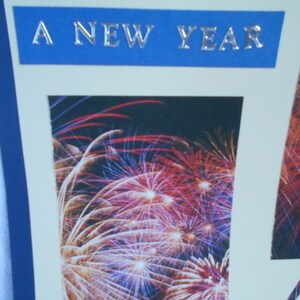 May include: A blue banner with the text "A New Year" in silver lettering, with a photo of fireworks in the background.
