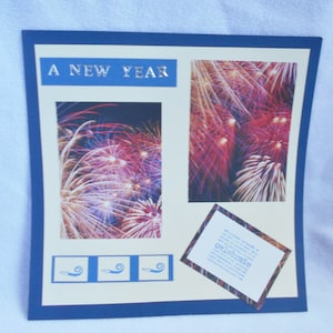May include: A New Year card with a blue border and a cream background. The card features two images of fireworks, a small card with the word "celebrate" and three blue party horn icons. The text "A New Year" is printed in silver on a blue background.
