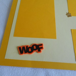 May include: A yellow and cream scrapbook page with a paw print and the text "King of the Yard". The word "Woof" is written in black letters on an orange background.
