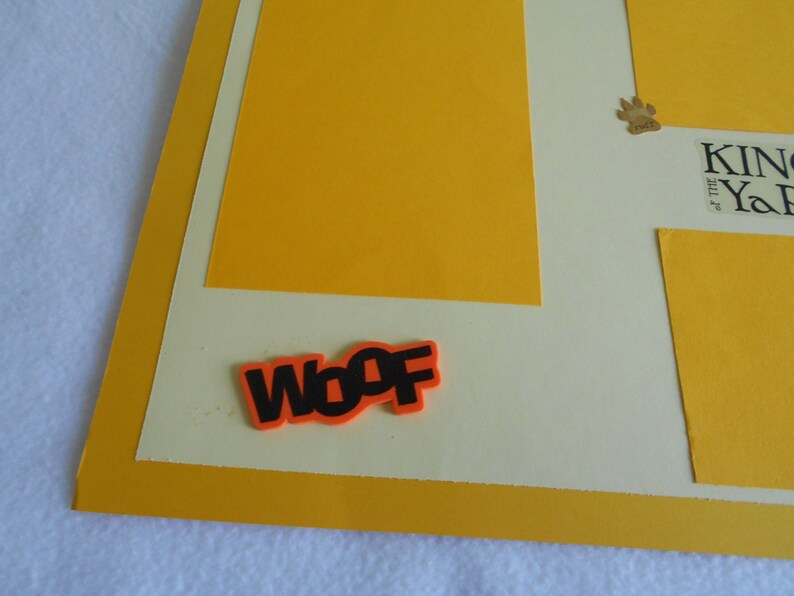 May include: A yellow and cream scrapbook page with a paw print and the text "King of the Yard". The word "Woof" is written in black letters on an orange background.