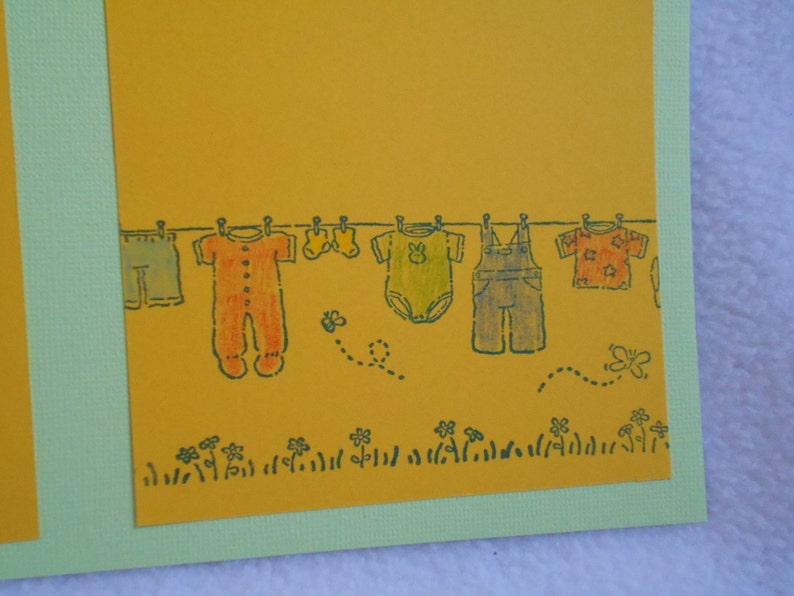 May include: A yellow card with a line of clothes hanging on a clothesline. The clothes include a pair of overalls, a long-sleeved onesie, a short-sleeved onesie, a pair of pants, and a short-sleeved shirt. There are also two butterflies and a bee on the card.