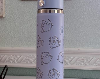 May include: A light purple Hydro Flask water bottle with a matching handle and lid. The bottle is covered in a pattern of smiling cartoon bear illustrations. The Hydro Flask logo is visible on the side.