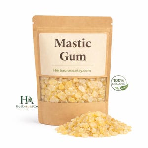 May include: A kraft paper bag with a clear window displaying Mastic Gum. The bag has a label with the text "Mastic Gum" and "Herbauraco.etsy.com". A pile of the yellow-beige gum is in front of the bag. A green circle with the text "100% ORGANIC" is on the right.