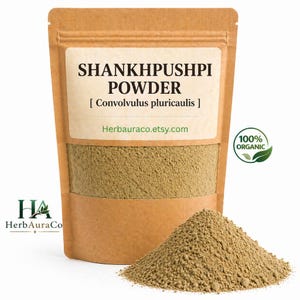 Op de afbeelding: Een bruine papieren zak met Shankhpushpi-poeder met een wit etiket. Op het etiket staat "SHANKHPUSHPI POWDER [Convolvulus pluricaulis]" en "Herbauraco.etsy.com". Een hoop poeder ligt voor de zak. Een groen "100% ORGANIC" logo staat rechts.