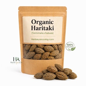 Puede incluir: Una bolsa de papel kraft marrón que contiene frutos secos orgánicos de Haritaki Terminalia chebula. La etiqueta presenta el texto Organic Haritaki, Terminalia chebula y herbauraco.etsy.com. Un pequeño montón de frutos ovalados y texturizados está delante.