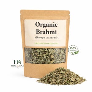 May include: A brown paper bag with a clear window filled with dried green Brahmi leaves. The label reads "Organic Brahmi (Bacopa monnieri)" and "Herbauraco.etsy.com". A small pile of the dried leaves is in front of the bag. A green leaf icon reads "100% Organic".