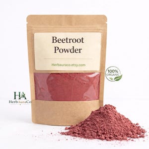 May include: A brown paper packet filled with vibrant red beetroot powder, with a clear window. The label reads "Beetroot Powder" and "Herbauraco.etsy.com". A small pile of the powder is in front of the packet. A green "100% Organic" sticker is visible.