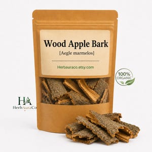 Op de afbeelding: Een bruine papieren zak met een doorzichtig venster met Wood Apple Bark. Het label luidt "Wood Apple Bark [Aegle marmelos]" en "Herbauraco.etsy.com". Een groene "100% ORGANIC" sticker staat rechts. Een stapel schors ligt voor de zak.