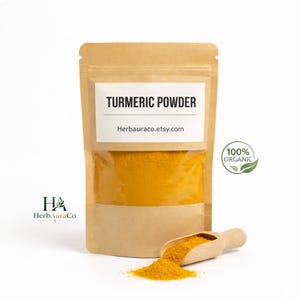 Puede incluir: Una bolsa de papel kraft llena de polvo de cúrcuma amarillo brillante. La bolsa tiene una ventana transparente y una etiqueta que dice "TURMERIC POWDER" y "Herbauraco.etsy.com". Una pequeña cuchara de madera y un montón de polvo de cúrcuma están frente a la bolsa. Un logo verde "100% ORGANIC" está a la derecha.