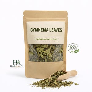 May include: A brown kraft paper pouch containing dried Gymnema leaves with a clear window. The label reads GYMNEMA LEAVES and Herbauraco.etsy.com. A small wooden scoop rests in front with a pile of loose leaves. A 100% ORGANIC seal is visible.