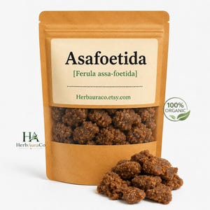 May include: A brown kraft paper pouch containing brown, textured chunks of Asafoetida resin. The label reads Asafoetida, Ferula assa-foetida, and herbauraco.etsy.com, with a 100% organic seal. A small pile of the resin chunks sits in front.