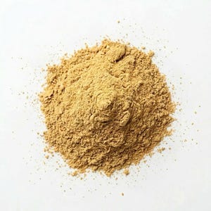 May include: A pile of light brown powder, possibly a spice or ingredient, sits against a white background. The powder has a fine, granular texture and appears to be freshly ground. The image is a top-down view, highlighting the texture and color of the powder.