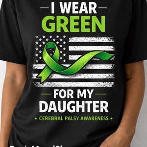 May include: Black t-shirt with a green ribbon and the text "I WEAR GREEN FOR MY DAUGHTER" over a white and black American flag design. The shirt also includes the text "CEREBRAL PALSY AWARENESS".