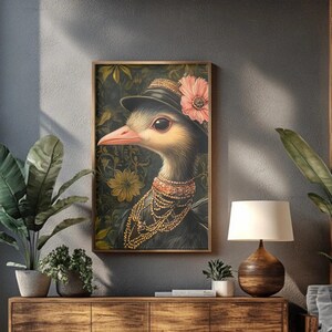 Puede incluir: Obra de arte enmarcada que presenta un avestruz con un sombrero negro adornado con una flor rosa y joyas doradas. El ave se encuentra sobre un fondo floral con una paleta de colores oscuros. La obra se exhibe en una habitación con muebles de madera y plantas.