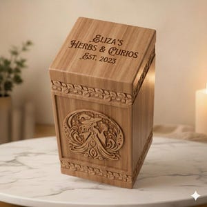 Pu&ograve; includere: Una scatola di legno marrone chiaro con il testo "Eliza's Herbs & Curios Est. 2023" inciso sulla parte superiore. La scatola presenta un disegno intagliato di una strega ed elementi celesti. La scatola ha motivi decorativi a foglie.
