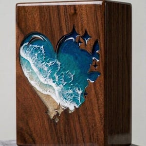 May include: A wooden box with a heart-shaped cutout filled with a resin ocean scene. The resin art depicts a beach with waves and stars. The box is made of dark wood and has a glossy finish.