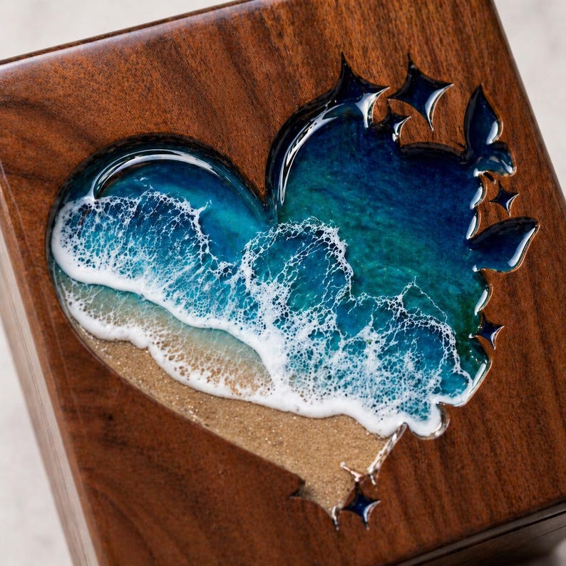 May include: A wooden box with a heart-shaped resin design depicting a beach scene. The resin features shades of blue and turquoise representing the ocean, with white waves crashing on a sandy shore. The box has a dark brown wood grain.