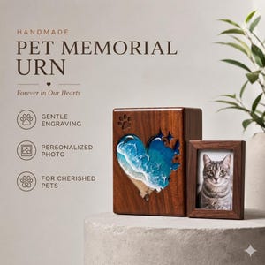 May include: A handmade pet memorial urn with a heart-shaped ocean design and a small photo frame. The urn is made of wood and features the text "PET MEMORIAL URN" and "Forever in Our Hearts". The frame holds a photo of a cat.