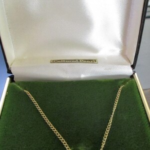 May include: A gold chain necklace with a single white cultured pearl pendant in a green velvet box. The box is labeled "12 KT. GOLD FILLED" and "Cultured Pearl".
