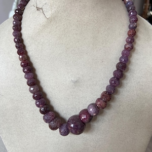 Könnte beinhalten: Eine Halskette aus facettierten, lila Edelsteinen. Die Halskette besteht aus einer Vielzahl von runden und ovalen Perlen in tiefen Lila- und Burgundertönen. Die Perlen sind zu einem schönen Schmuckstück aufgefädelt.