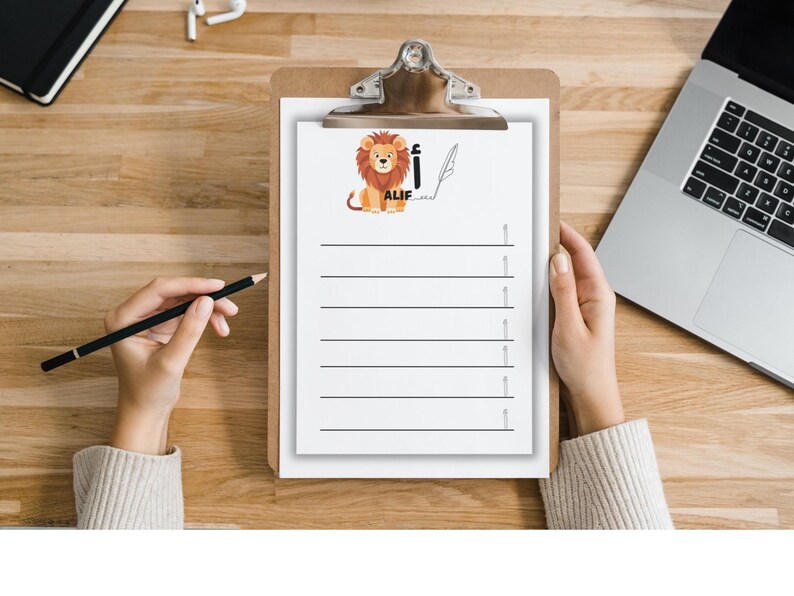 May include: A clipboard with a white paper featuring a cartoon lion illustration and the word "ALIF". The paper has horizontal lines for writing. A hand holds a black pencil, and another hand holds the clipboard.