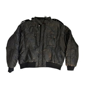 May include: A black quilted bomber jacket featuring a high collar, a front zipper closure with snap buttons, two chest pockets, two side pockets, and shoulder epaulets. The jacket has ribbed cuffs and a ribbed hem, providing a structured fit.
