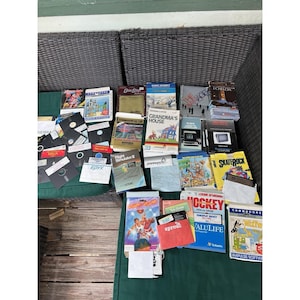 May include: A collection of vintage Commodore 64 computer software, including various game boxes, manuals, and floppy disks. Titles visible include Grandma's House, Flight Simulator II, Skaterock, Slam Dunk, and Powerplay Hockey, featuring colorful graphic art.