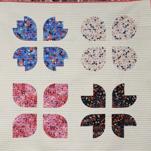 May include: A white quilt with a geometric pattern of circles and leaves. The circles are in shades of pink and white, and the leaves are in shades of blue, pink, and black. The quilt is edged with a red border. The text "@HAPPYSEWLUCKY" is printed in the bottom left corner.