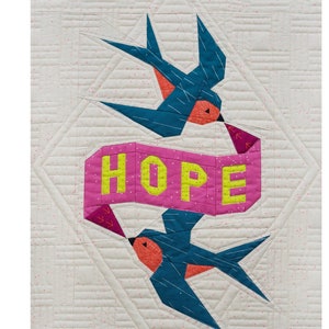 Op de afbeelding: Een roze banner met het woord "HOPE" in gele letters, met twee blauwe vogels die boven en onder de banner vliegen. De achtergrond is een witte stof met een subtiel roze stippenpatroon.