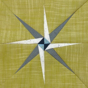 Può includere: Un blocco di trapunta a forma di stella di colore bianco, grigio e blu su uno sfondo verde.