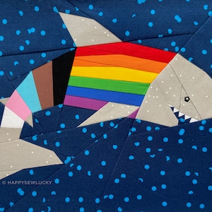 May include: A colourful patchwork quilt design of a shark swimming in a blue ocean with white polka dots. The shark is made of different coloured fabric pieces, including a rainbow stripe across its back. The quilt is signed "HAPPYSEWLUCKY" in the bottom left corner.