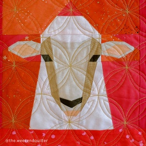 Op de afbeelding: Een witte schapenapplique met een bruine neus en zwarte ogen, gestikt op een rode achtergrond met een gouden bloemenpatroon.