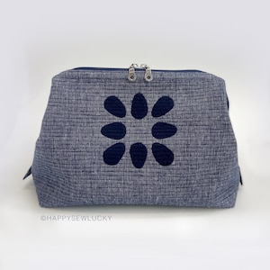 May include: A dark blue zippered pouch with a black flower design. The pouch is made of a textured fabric and has a silver zipper.