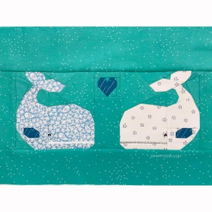 May include: Two whale-shaped fabric patches on a turquoise background with white polka dots. The whale on the left is blue with a white and blue floral pattern. The whale on the right is white with a white and blue polka dot pattern. A small blue heart with white stripes is in the center of the image. The text "@HAPPYSEWLUCKY" is in the bottom right corner of the image.