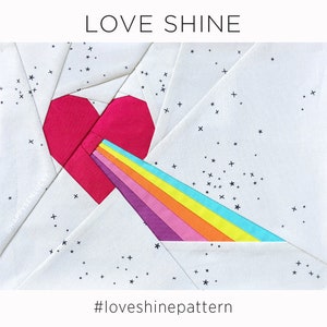 Puede incluir: Un bloque de colcha de tela blanca con un corazón rojo y un arcoíris que irradia de él. El fondo es blanco con estrellas negras. El texto "LOVE SHINE" está en la parte superior del bloque y "#loveshinepattern" en la parte inferior.