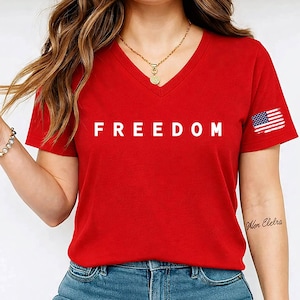 A woman wearing a red t-shirt with the word "FREEDOM" printed on it, along with a necklace and a tattoo on her arm.