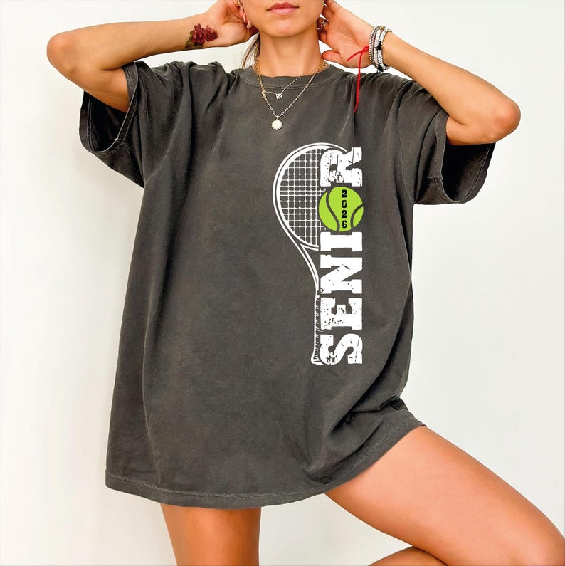 A person wearing a grey t-shirt with a tennis racket graphic and the word "SEASON" printed on it.