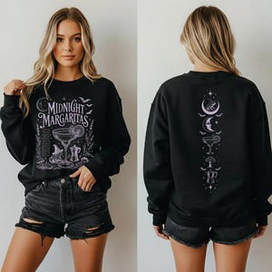 May include: A black long-sleeve sweatshirt featuring a white graphic print. The front displays a margarita glass, a witch hat, and the text "MIDNIGHT MARGARITAS". The back features a vertical design of a crescent moon, a cocktail, and a mushroom.