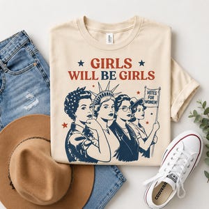 a casual outfit consisting of a beige t-shirt with a graphic design, a pair of blue jeans, a brown hat, and a pair of white sneakers.
