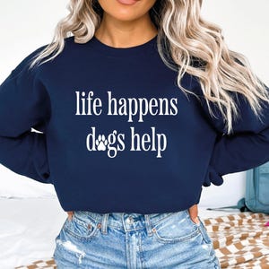 A woman wearing a navy blue sweatshirt with the text "life happens dogs help" printed on it.