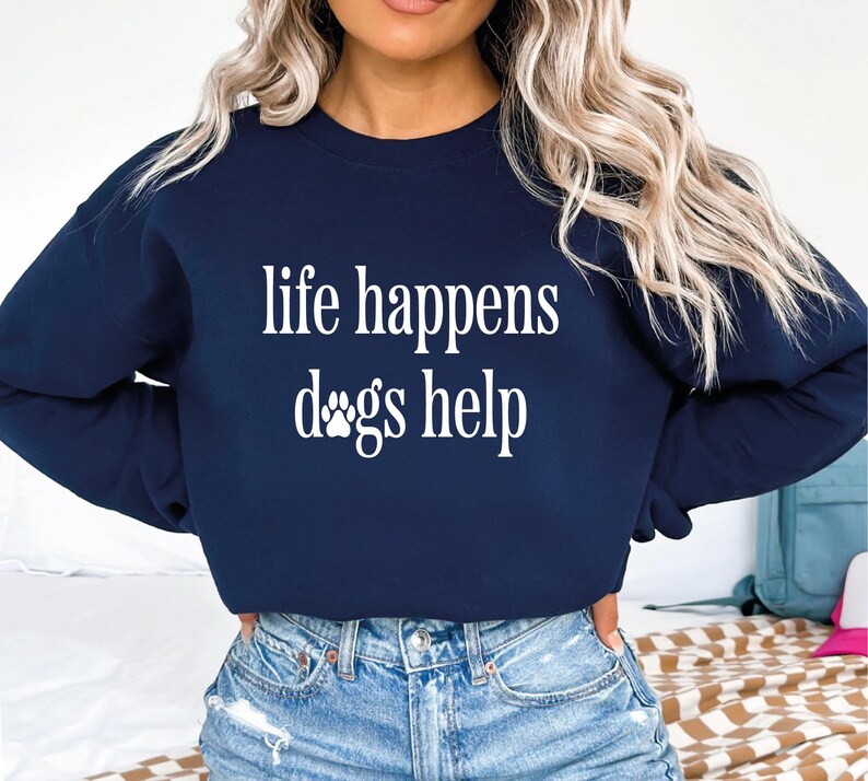 A woman wearing a navy blue sweatshirt with the text "life happens dogs help" printed on it.