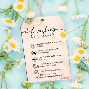 a wooden tag with instructions for washing clothes, placed against a background of white and yellow flowers.