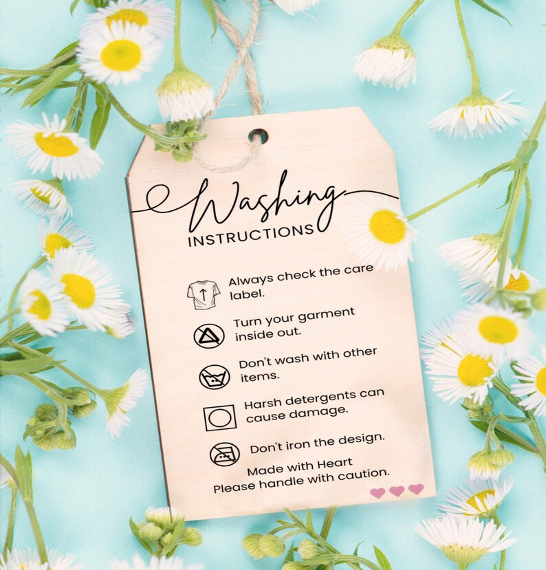 a wooden tag with instructions for washing clothes, placed against a background of white and yellow flowers.