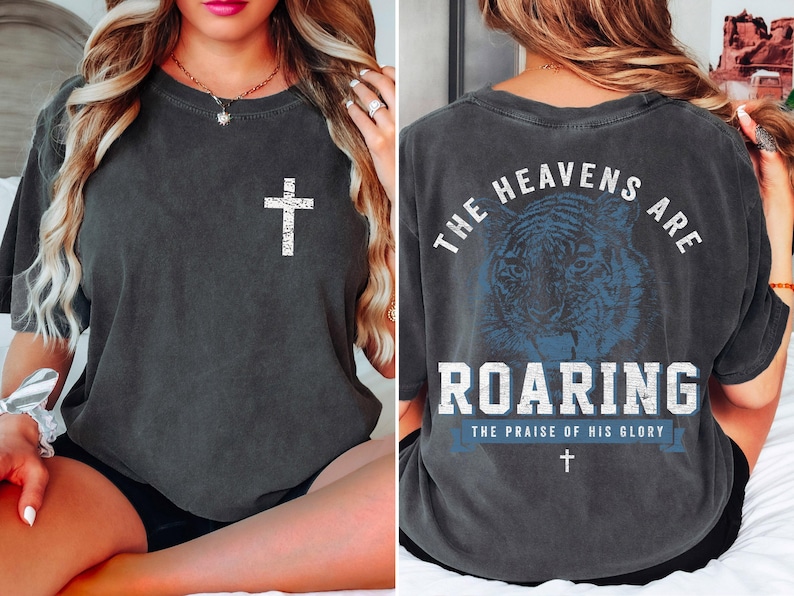 The image is a collage of two photos. In the left photo, a woman is sitting on a bed with her hair in a ponytail. In the right photo, the back of a gray t-shirt is shown, featuring a graphic design of a tiger and the text "The heavens are roaring" along with the phrase "The praise of his glory".