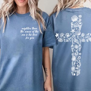 A woman wearing a blue t-shirt with a white cross design and text on the front and back.